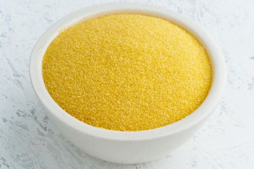 Corn, polenta in a white bowl on white background. Dried cereals in cup, vegan food, fodmap diet. Side view, close up.