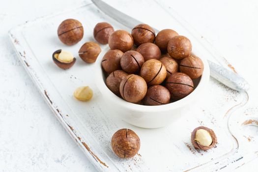 Plate with almonds in endocarp, whole and chopped open nuts in bulk on a cutting board with knife on a white background, side view.