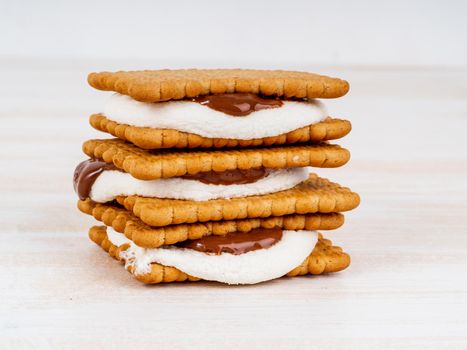 Smores, marshmallow sandwiches - traditional American sweet chocolate cookies on white wooden table, side view.