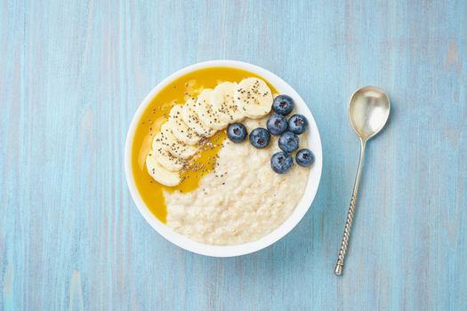 Oatmeal with bananas, blueberries, chia seeds, jam on blue wooden background. Top view. Healthy breakfast