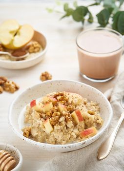 Oatmeal with apple, nuts, cinnamon, honey and cup of hot chocolate on white wooden light background. Vertical. Healthy diet breakfast