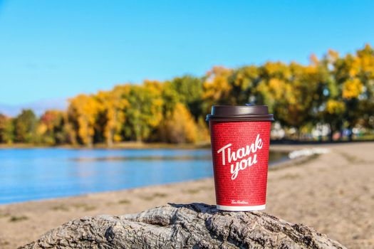 Red Paper Tim Hortons cup of coffee with Thank You words on natural morning background. Fresh morning