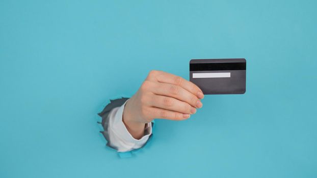 A woman's hand sticking out of a hole in a paper blue background holds a credit card