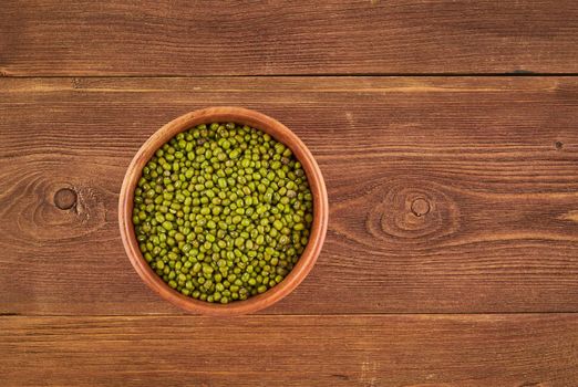 Mung beans in wooden bowl on brown background, top view, copy space, close up