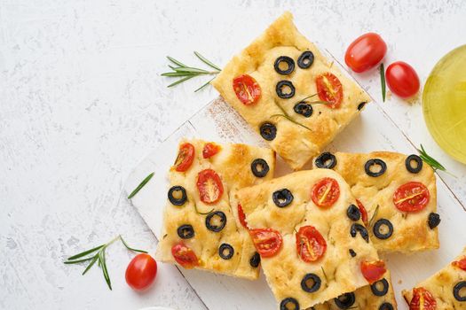 Sliced pieces of a focaccia with tomatoes, olives and rosemary. Copy space for text. Traditional Italian flat bread. Top view.