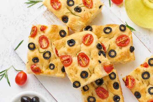 Sliced pieces of a focaccia with tomatoes, olives and rosemary. Traditional Italian flat bread. Top view.