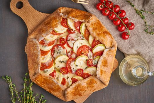 Homemade galette with vegetables, wholegrain pie with tomatoes, zucchini, cheese. Top view. Dark brown table