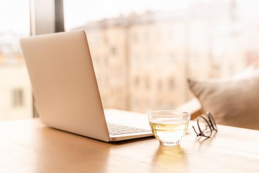 Freelance Desk with open laptop, cup of green tea and glasses on table. Cafe or coworking space. Concept of digital nomads, home office, blogging. No people.
