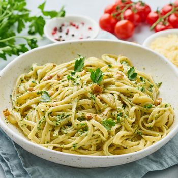 Pesto pasta, bavette with walnuts, parsley, garlic, nuts, olive oil. Side view, close-up, blue background