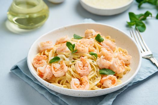 Pasta spaghetti with grilled shrimps, bechamel sauce, mint leaf on blue table, italian cuisine, side view