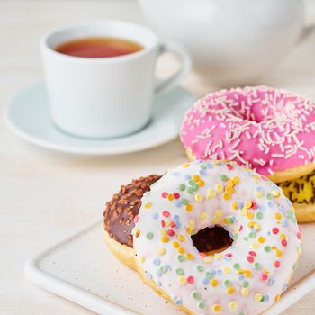 Doughnuts and tea. Bright, colorful junk food. Light beige wooden background. Side view, close up.