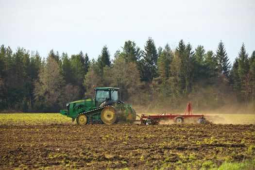 Crawler Tractor on farm plowing ploughing field with Harrow in Spring Kicking up Dust Clouds from Soil. High quality photo