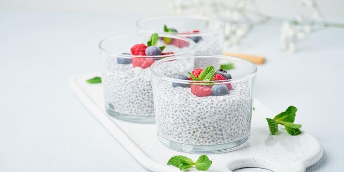 Banner with chia pudding with fresh berries raspberries, blueberries. Three glass, light background, side view, flowers