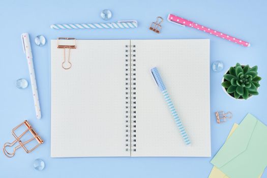 Blank notepad page in bullet journal on bright blue office desktop. Top view of modern table with notebook, stationery. Mock up, copy space, concept for diary, top view