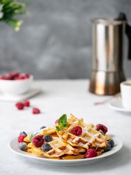 Belgian waffles with raspberries, blueberries, curd and coffee, side view, vertical. Healthy homemade breakfast, light concrete background