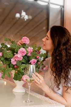 Dreaming woman with glass of alcoholic white wine in cafe in summer terrace and bouquet of roses on the table