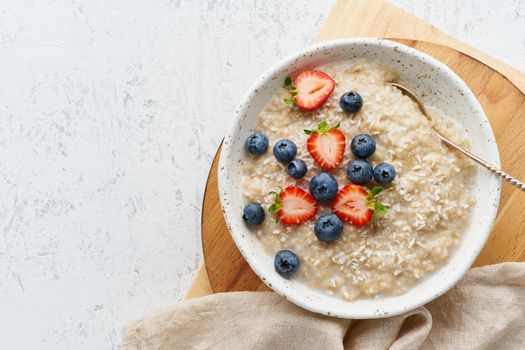 Oatmeal rustic porridge with blueberry, bilberry, blackberry, strawberry, dash diet, wooden white background top view copy space