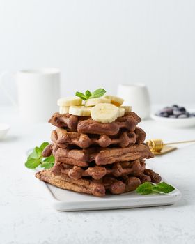 Chocolate banana waffles with maple syrup on a white table, side view, vertical. Sweet brunch