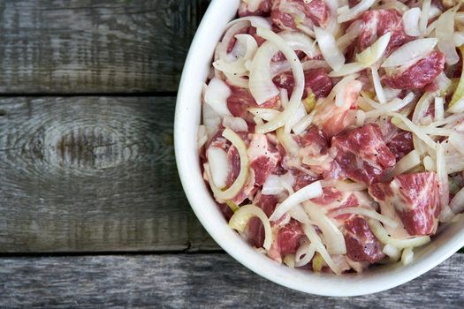 marinated meat with onion rings on the dark wooden background with copy space top view in the deep white dish pan