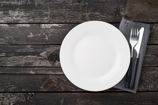 clean empty white plate, fork and knife on a gray old rustic wooden table, copy space, mock up, top view.