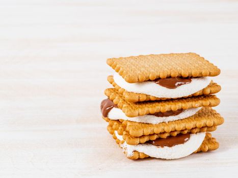 Smores, marshmallow sandwiches - traditional American sweet chocolate cookies on white wooden table, side view.