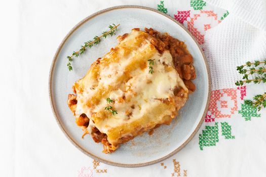 Cannelloni pasta with filling of ground beef, tomatoes, baked with bechamel tomato sauce and mozzarella. Classical Italian cuisine, white tablecloth with embroidery, rustic style, top view, close up