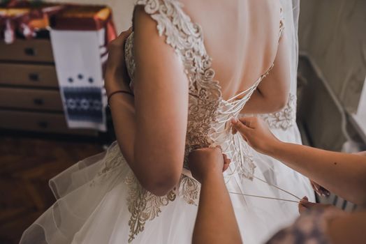 The back of the bride in a wedding dress. Mom's and woman's hands help fasten the clasps at the back.