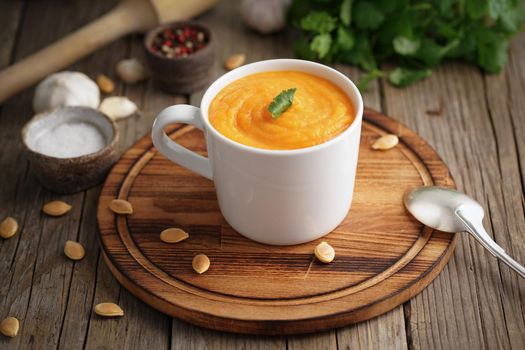 Dietary vegetarian lunch on cutting board with parsley, garlic. Pupmkin cream soup puree in cup on brown wooden table, side view.