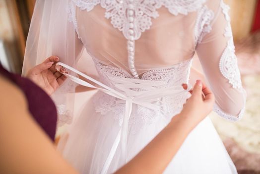 The back of the bride in a wedding dress. Mom's and woman's hands help fasten the clasps at the back.