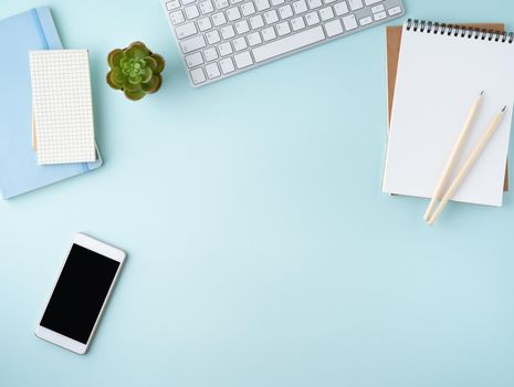 Top view of modern blue office desktop with blank notepad, computer, smartphone. Mock up, empty space
