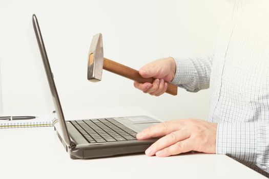 The man raised a hammer over the computer, the man in the shirt wants to break the laptop. The concept of fatigue from work