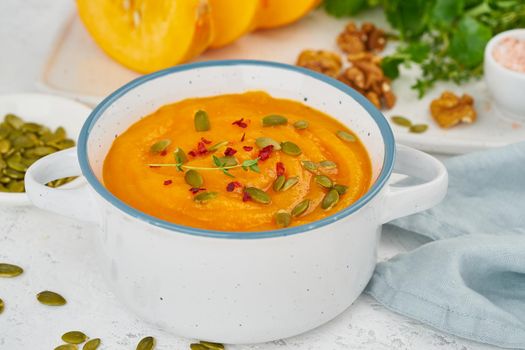 Pumpkin vegetarian cream soup with walnuts, side view on light background closeup