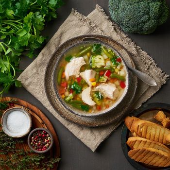 Homemade chicken soup with vegetables, broccoli on a dark brown background, top view