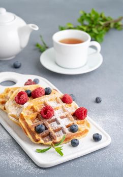 Belgian waffles with raspberries, blueberries, tea, vertical. Healthy homemade breakfast, blue background