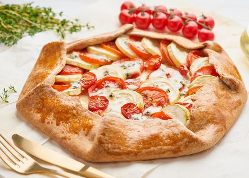 Homemade galette with vegetables, wholegrain pie with tomatoes, zucchini, cheese.Side view. Light white wooden table
