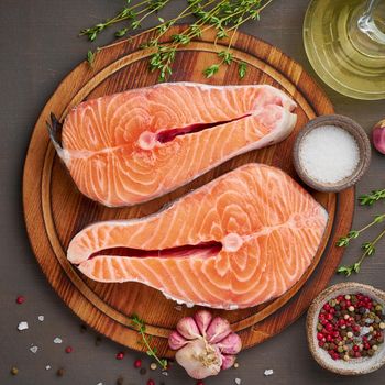 Two salmon steaks, top view, close up. Fish fillet, large sliced portions on chopping board on dark table.