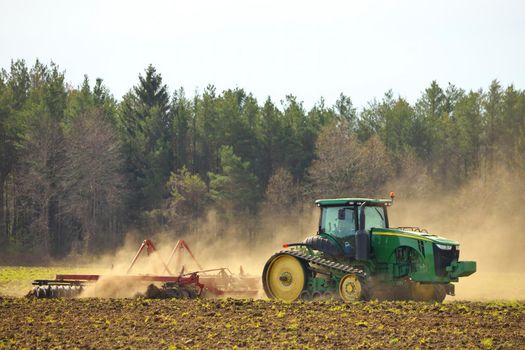 Crawler Tractor on farm plowing ploughing field with Harrow in Spring Kicking up Dust Clouds from Soil. High quality photo