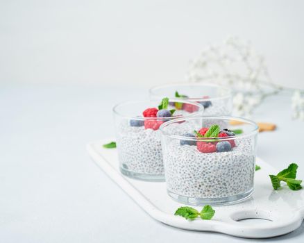 Chia pudding with copy space, fresh berries raspberries, blueberries. Three glass, light background, side view, flowers