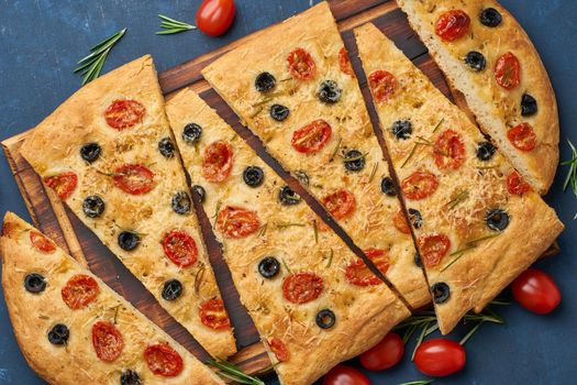 Focaccia, pizza, italian flat bread with tomatoes, olives and a rosemary on dark blue table, top view