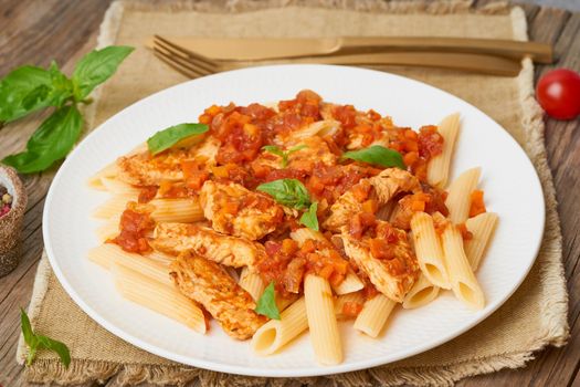 Penne pasta, chicken or turkey fillet, tomato sauce with basil leaves on old rustic wooden background