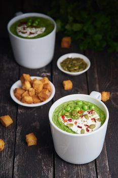 Broccoli cream soup, vertical on dark wooden background. Vegetable green puree in two large white cup. Diet vegan soup of broccoli, zucchini, green peas