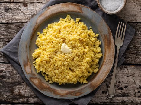 Bulgur wheat. Boiled bulghur cereal in plate on dark old wooden table. Healthy vegetarian food, top view