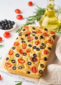 Focaccia with tomatoes, olives and a rosemary, vertical. Whole Italian flat bread, bottle with oil