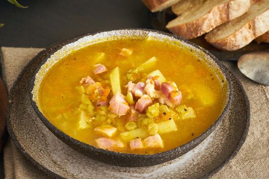 Winter hot soup with chopped green peas, pork, bacon, smoked on a dark brown wooden table. Delicious appetizing fat rich soup, close up, side view
