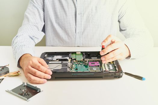 Man repairs computer. A service engineer in a shirt repairs a laptop, at a white Desk against a white wall, flare.