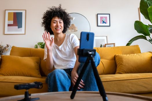Happy African American mixed race female vlogger waves hand during vlog. Latina woman greets friend during video call using mobile phone. Social media and technology concept.