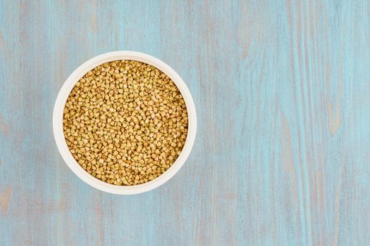 green buckwheat in white bowl on blue wooden table, gluten free wholegrain, fodmap diet, copy space