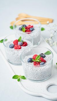 Chia pudding with fresh berries raspberries, blueberries. Three glass, vertical, light background, side view, flowers