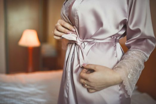 Young thin woman in pink silk robe unties the belt with her hands. bride in morning clothes