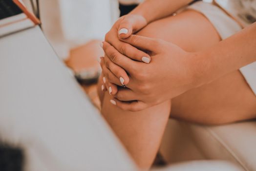 The girl sits with her legs crossed at a white cosmetic table. The bride in a white wedding dress with an open neckline. Various professional cosmetics hairbrush female accessories laid out on the tab